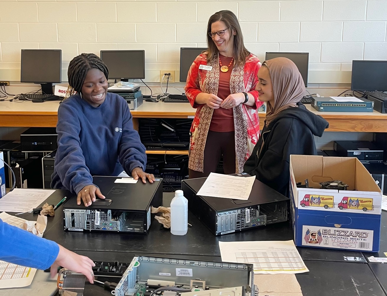 Melanie Merin talking with two female students in a cyber tech class who are assembling a desktop computer